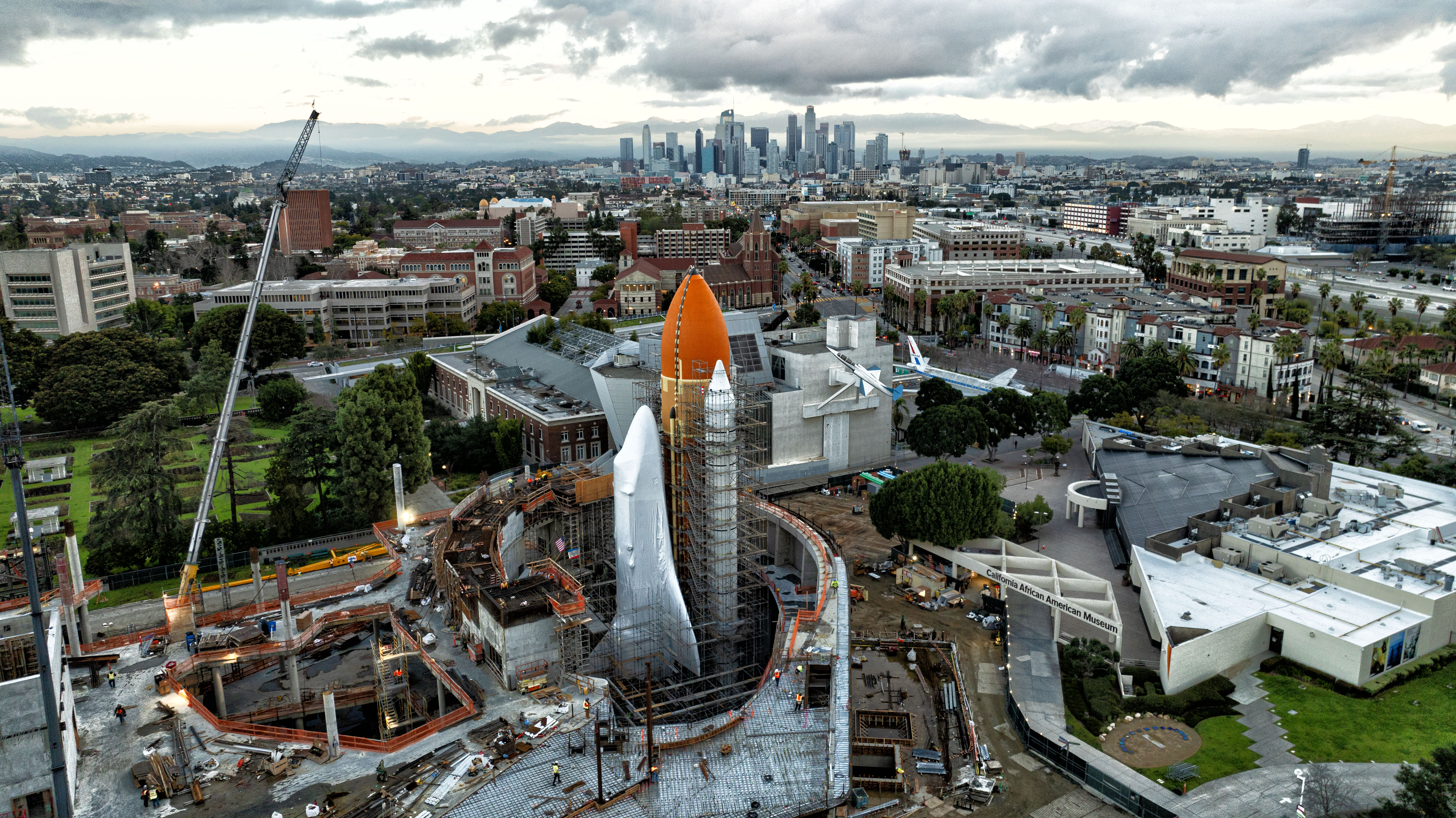 Aerial shot of full space shuttle stack in the future Samuel Oschin Air and Space Center with downtown downtown LA skyline  and gray clouds in the background.