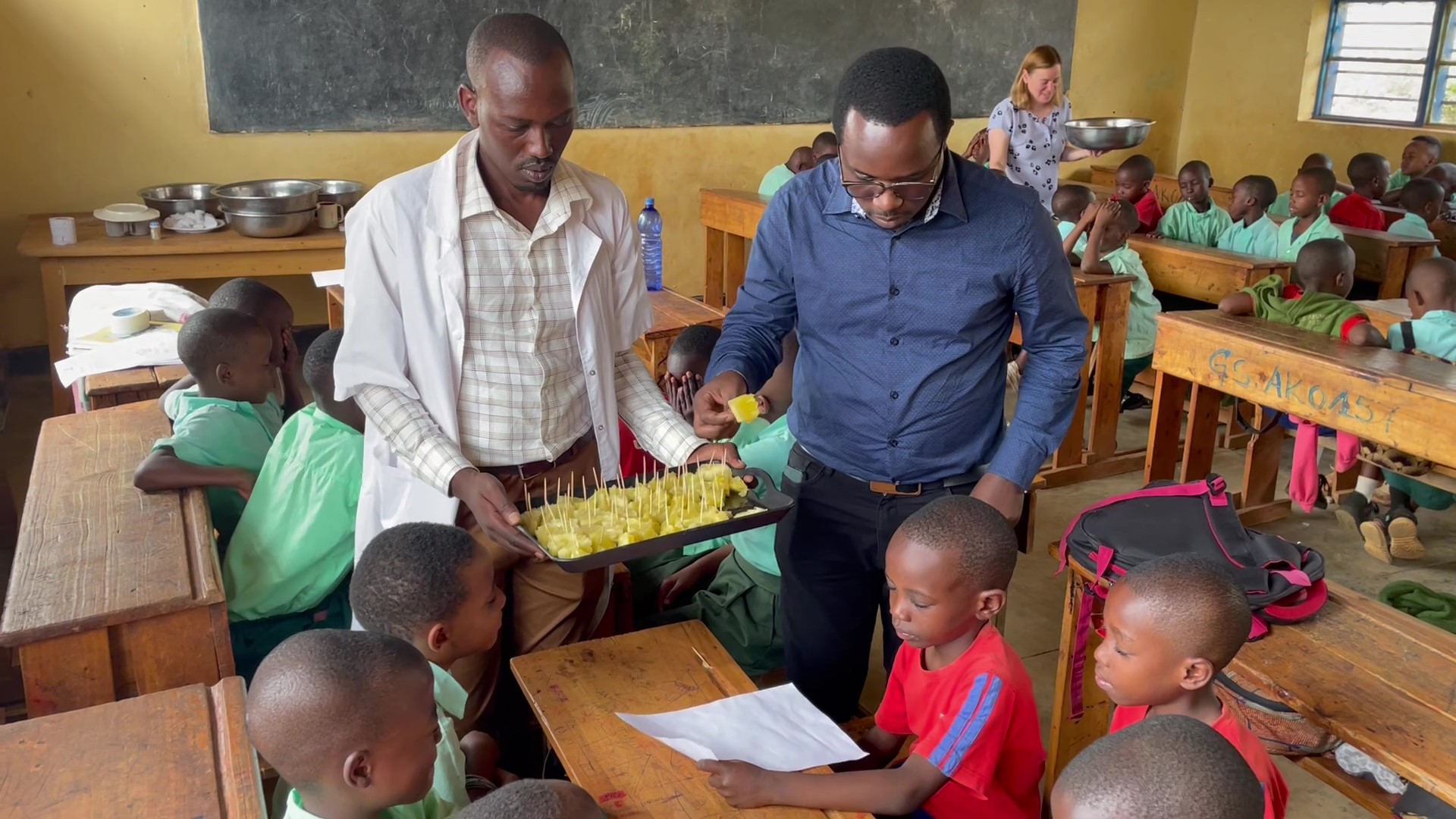 Two men hand out pineapple sticks to students during a science class