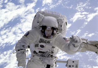 An astronaut conducts a spacewalk with Earth visible behind him.