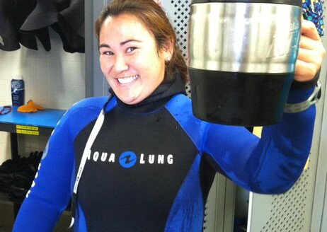 Wearing a wetsuit with her hair pulled back as she stands in the California Science Center's dive locker, Erin Shusterman holds her coffee mug in a gesture that seems to say "cheers" 