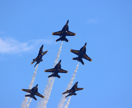 The Blue Angels soar through a nearly cloud-free, crystal blue sky, sailing upwards into the air in formation.
