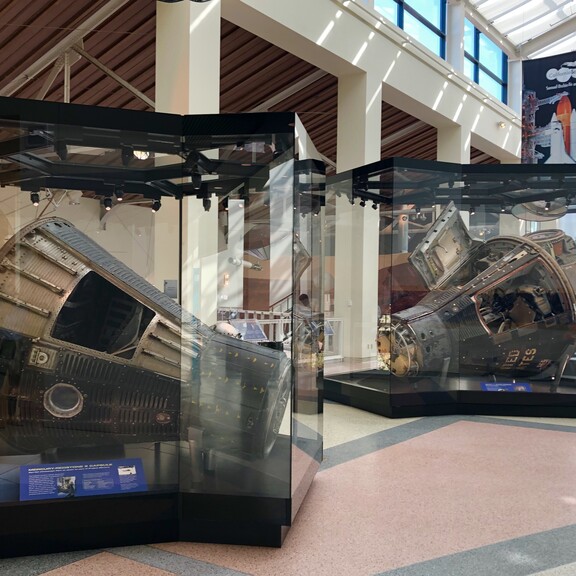 One Mercury, one Gemini, and one Apollo space capsule, each on display in its own glass case