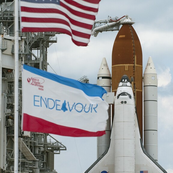 Space Shuttle Endeavour on the launch pad, with the American flag and an Endeavour flag in the foreground