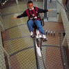 A boy balances a bike on a wire, three stories above the floor below.