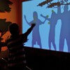 People stand in front of a wall-sized screen. Their shadows are projected onto the screen for an interactive game.