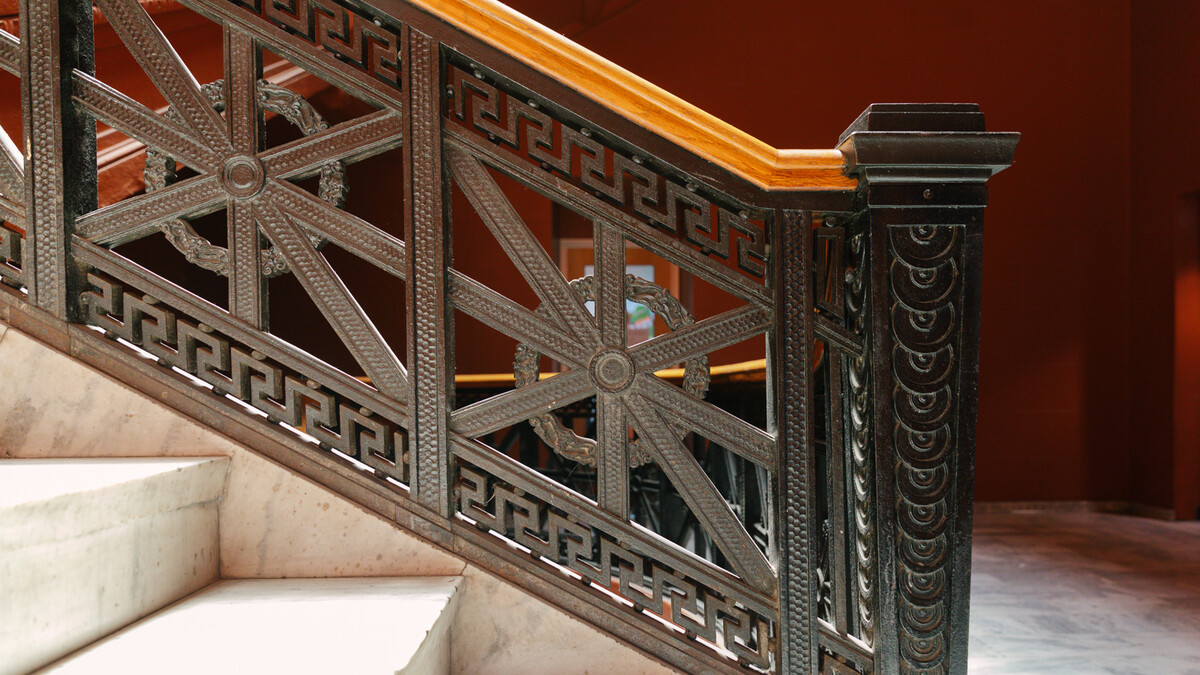 Black intricate stair rail and white marble stairs sit in front of burnt orange Wallis Annenberg Building stairway walls