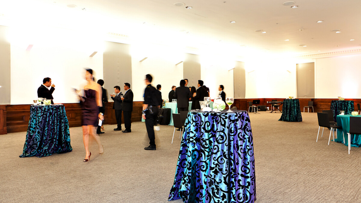 Event guests in formal attire drink cocktails in MUSES Room among black and teal patterned cocktail tables