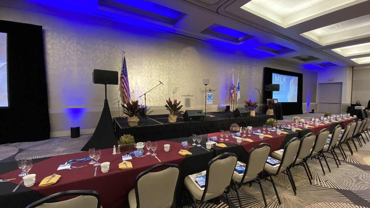 Long VIP head table lined in burgundy, black, and gold facing stage flanked by projector screens in Loker Conference Center