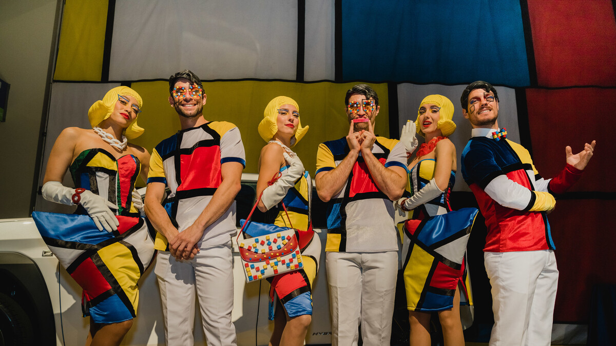 Three female and 3 male entertainers wearing Mondrian inspired costumes  and LEGO minifigure inspired wigs pose in front of Lexus and Mondrian print backdrop