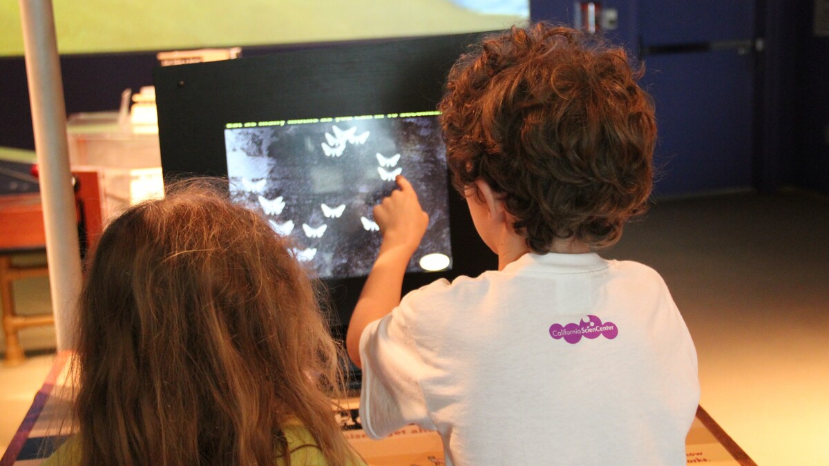 Two kids gather in front of a screen to play a game.