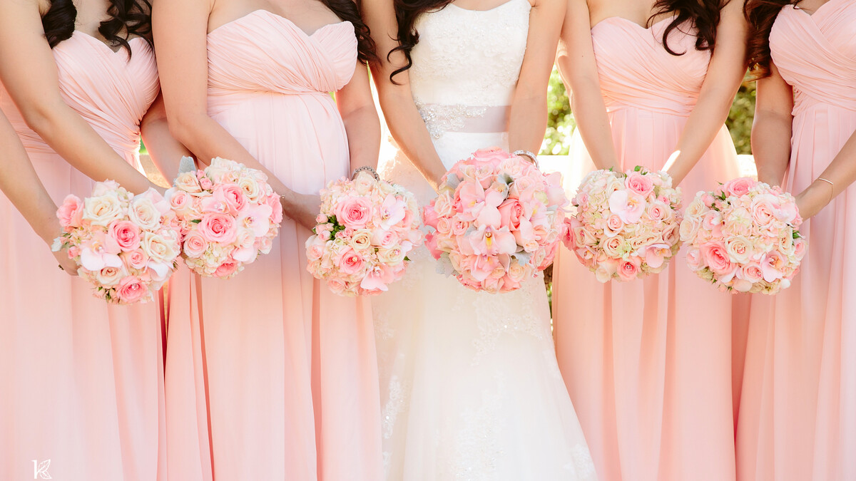 Bridesmaids in long pink dresses holding bouquets flank a bride in white 
