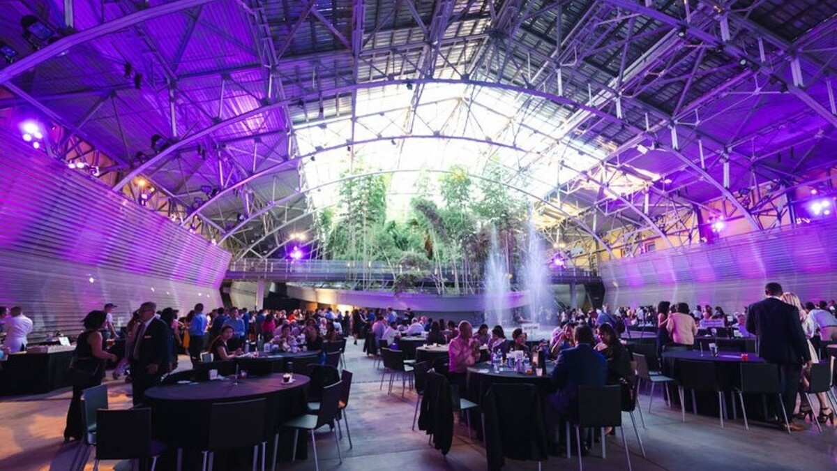 Guests are seated for a gala in the Wallis Annenberg Building. The event space has a fountain and purple-hued accent lighting.