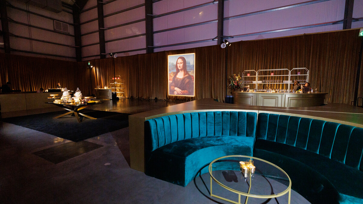 Pavilion hangar space outfitted with perimeter drapery and set with plush lounge furniture and oversized Mona Lisa for a gala after party