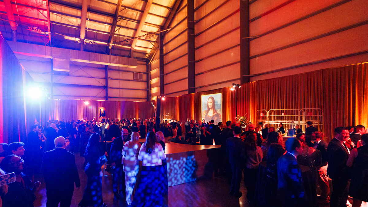 Pavilion hangar space outfitted with perimeter drapery and illuminated in orange and amber. Event space is filled with guests enjoying after party activities.