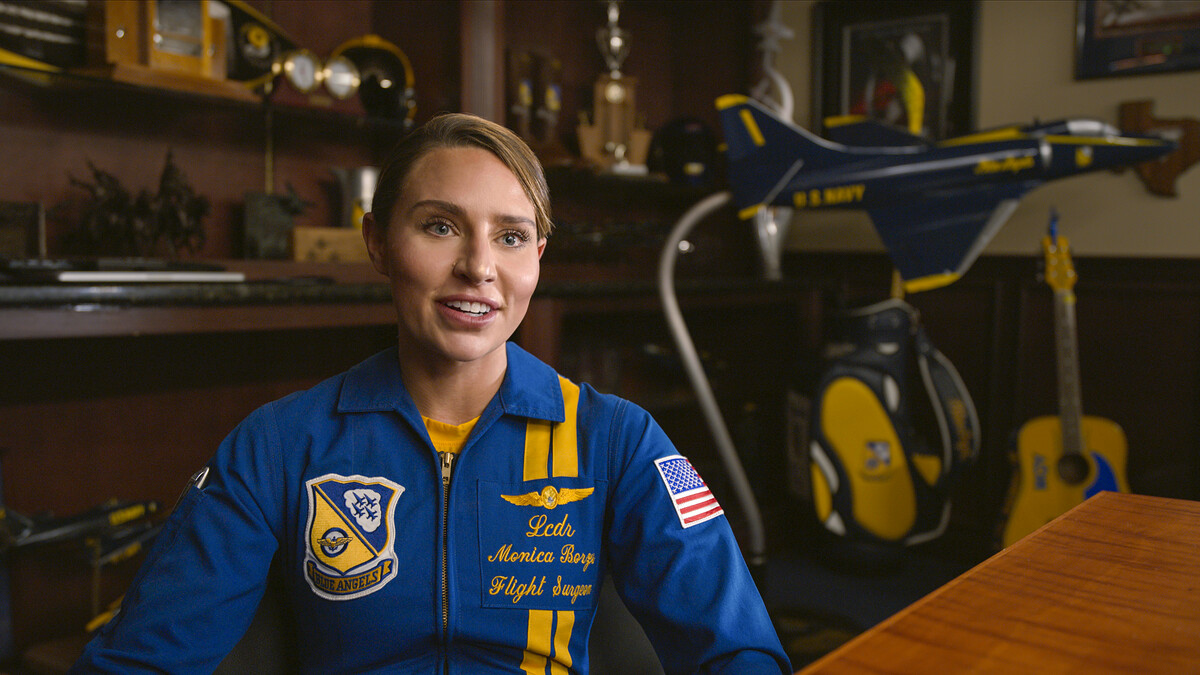 A female Blue Angels pilot sits at a desk.