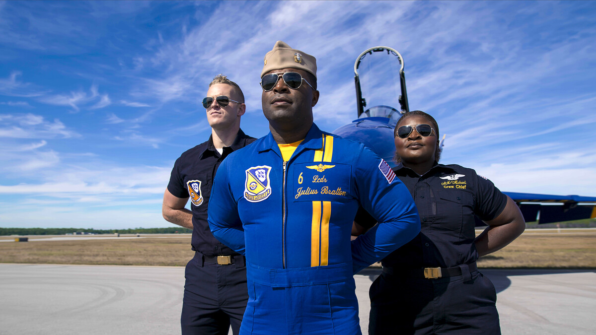Blue Angels pilot and crew pose in position in front of plane.