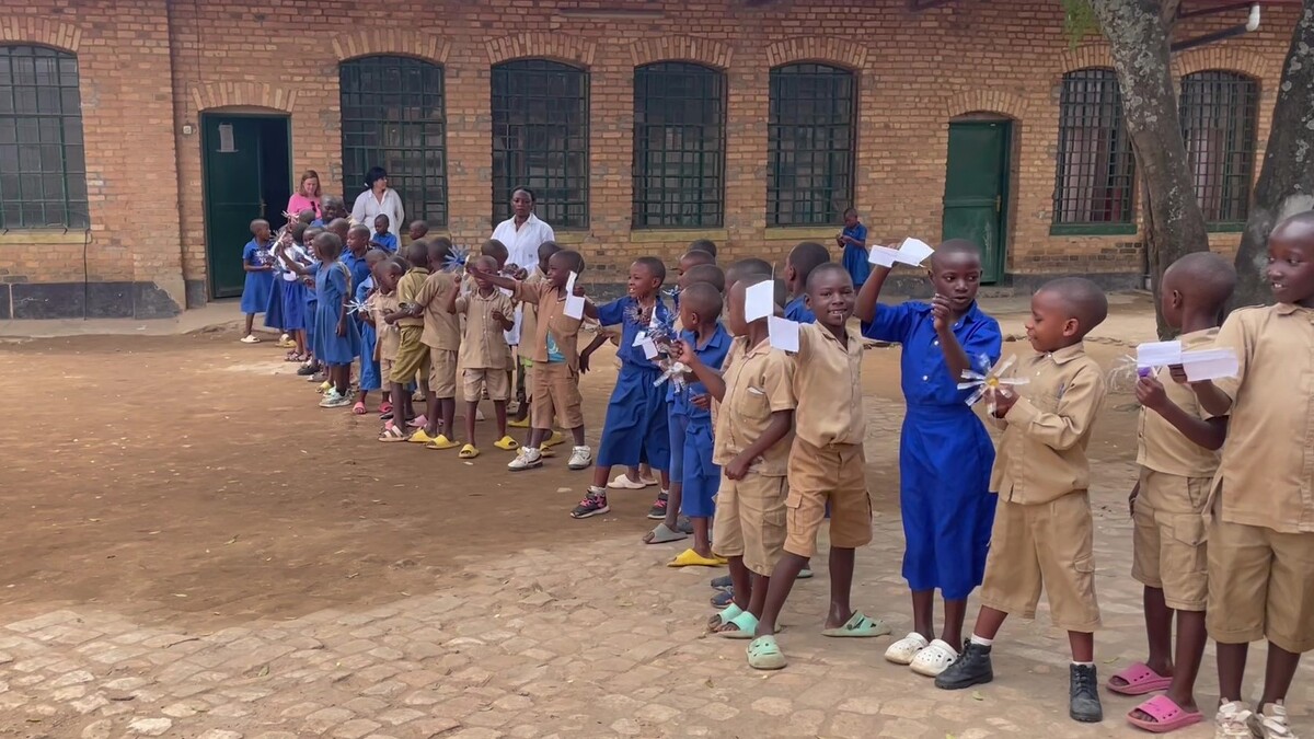 Students in brown and blue stand in a line outside holding small paper wings