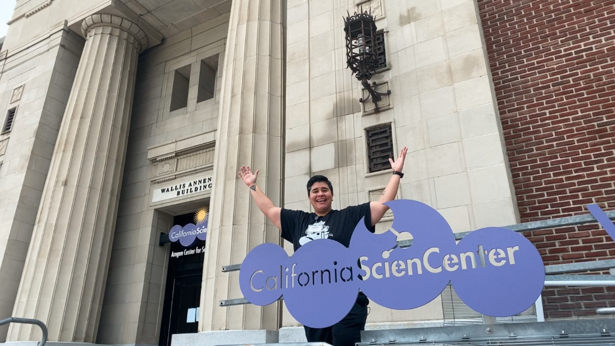 Educator Monica in front of Wallis Annenberg Building holding hands in the air.