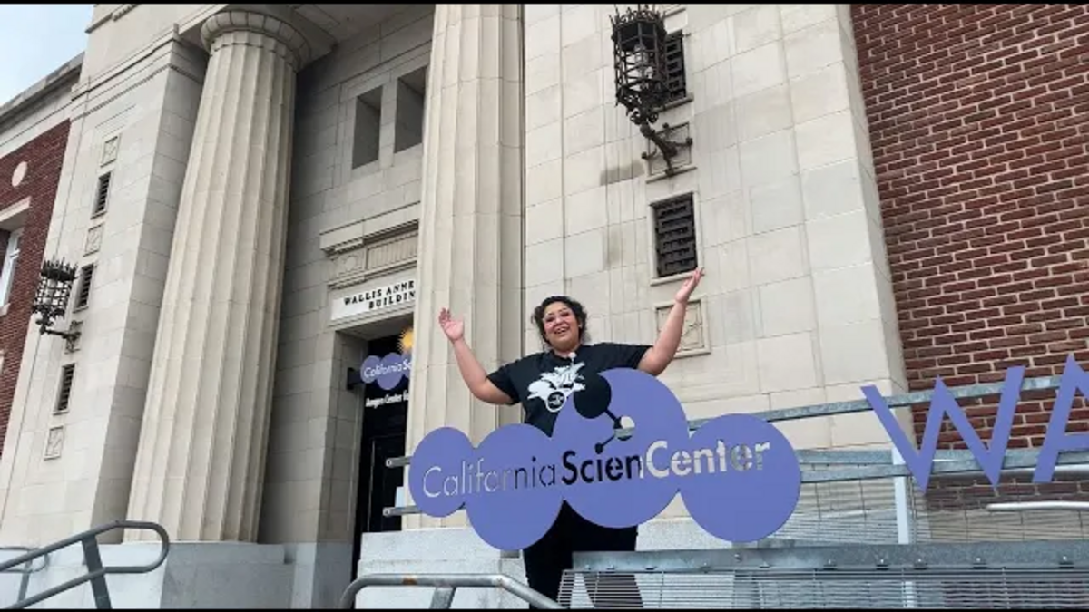 Educator Mariela in front of Wallis Annenberg Building holding hands in the air.