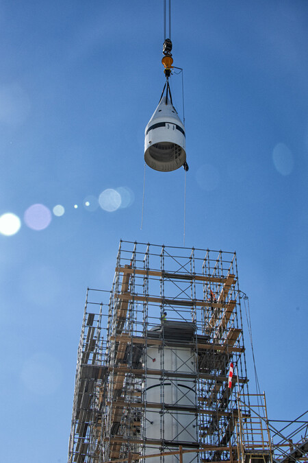 Forward assembly is hoisted above a solid rocket motor, which is surrounded by scaffolding. Blue sky is visible in the background.