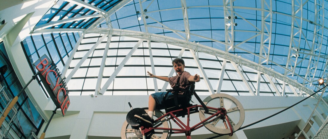 Aided by physics, a boy with outstretched arms balances a bike on a wire.