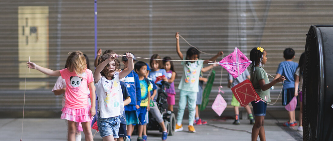 Young kids wait in line to fly their kites near a large fan while at Hands-On Science Camp