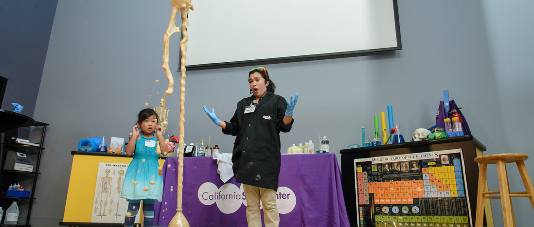 Education staff member and child watch wide-eyed as mentos coke bottle experiment explodes in front of them
