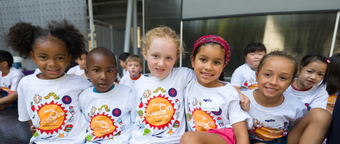 Young kids wearing Hands-On Science Camp shirts sitting in row posing for photo