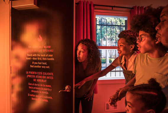 A family peers into a fiery-looking space behind a door in the Fire! Science & Safety exhibition.